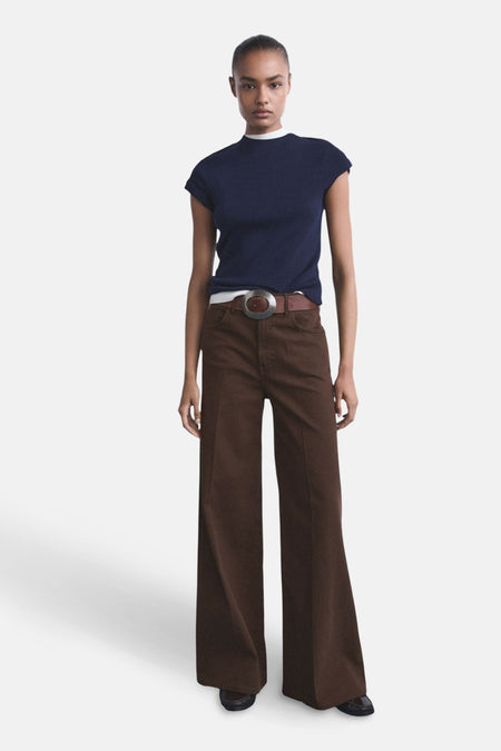 Jeans colorés marron by MANGO, de coupe évasée, portés avec une ceinture marron et un t-shirt bleu marine.
