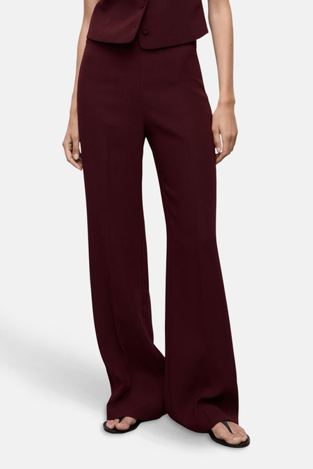 Pantalon de costume bordeaux de MANGO, coupe évasée, porté avec des sandales noires.