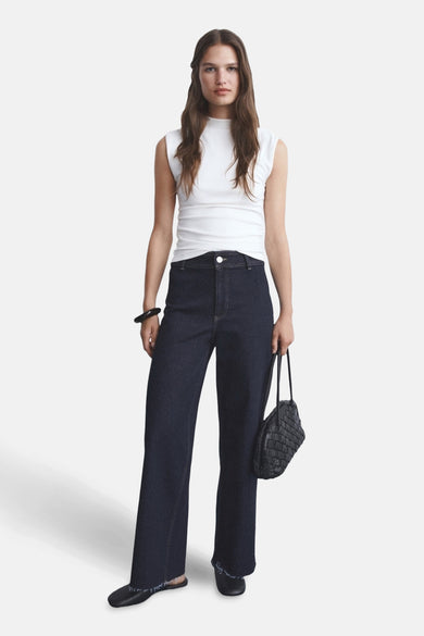 Jean large en denim bleu foncé de MANGO, avec ourlets effilochés, porté avec un haut blanc et un sac noir tressé.