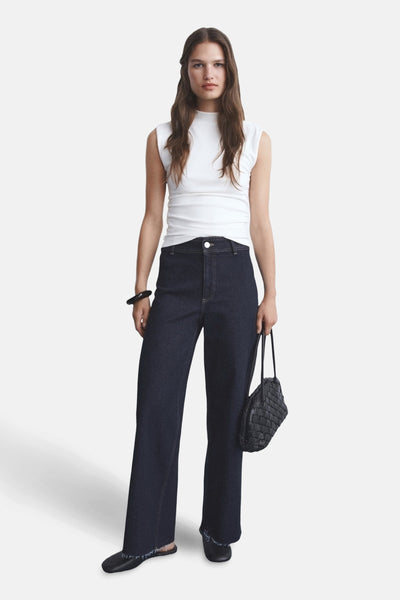 Jean large en denim bleu foncé de MANGO, avec ourlets effilochés, porté avec un haut blanc et un sac noir tressé.