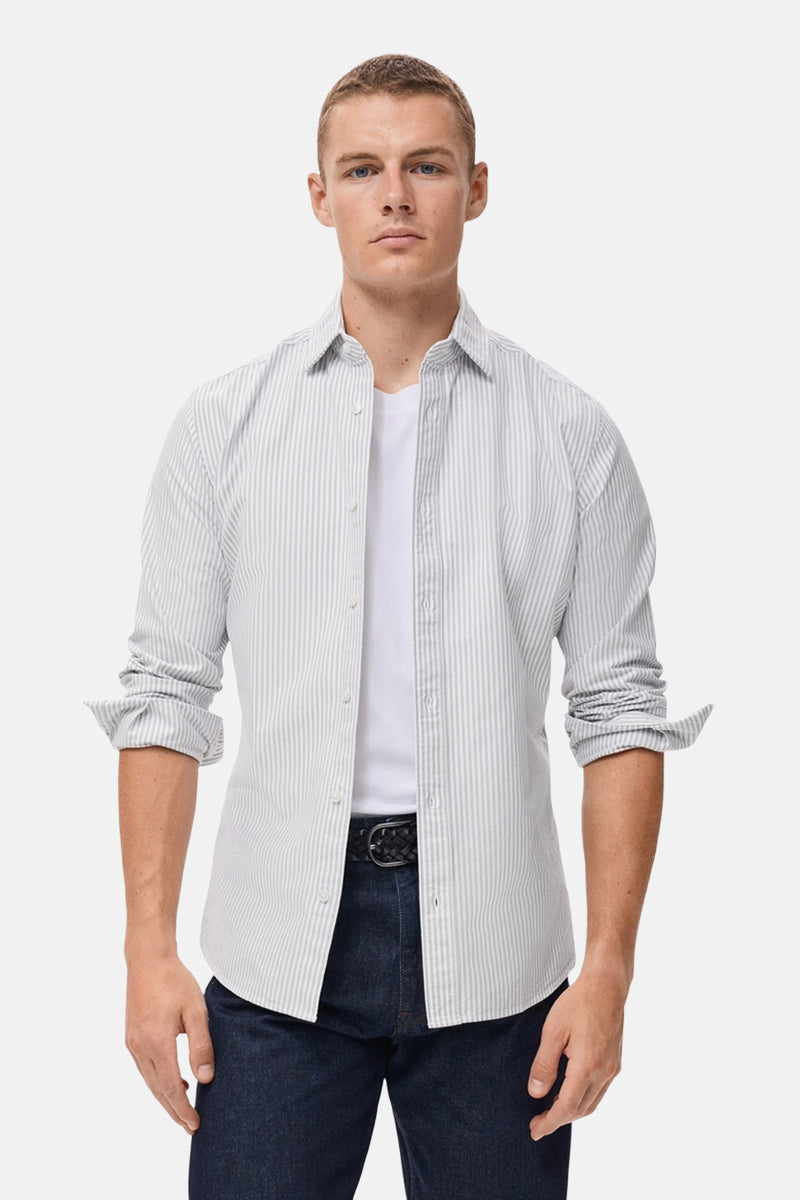 Gestreepte, veelkleurige blouse met lange mouwen van MANGO, gedragen open over een wit T-shirt en een blauwe jeans.