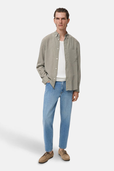 Kaki gestreept overhemd van MANGO, gedragen open over een wit T-shirt en een lichtblauwe jeans.