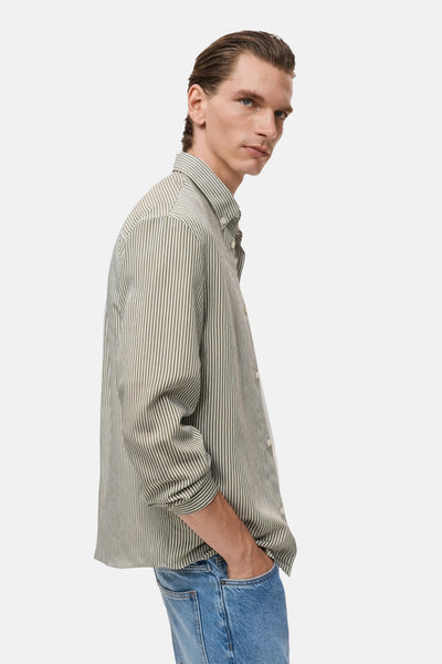 Chemise kaki à rayures verticales de MANGO, portée avec un jean bleu, vue de profil.
