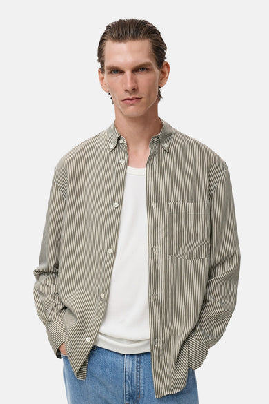 Kaki overhemd met lange mouwen van MANGO, met verticale strepen, gedragen over een wit T-shirt en een blauwe jeans.