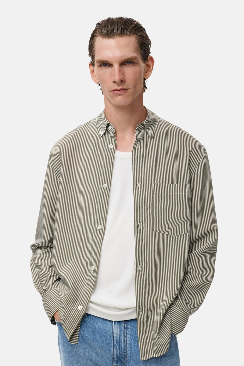 Kaki overhemd met lange mouwen van MANGO, met verticale strepen, gedragen over een wit T-shirt en een blauwe jeans.