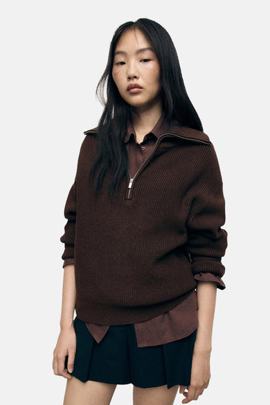 Bruine coltrui van MANGO, met zilveren ritssluiting, gedragen over een zwarte blouse en rok.
