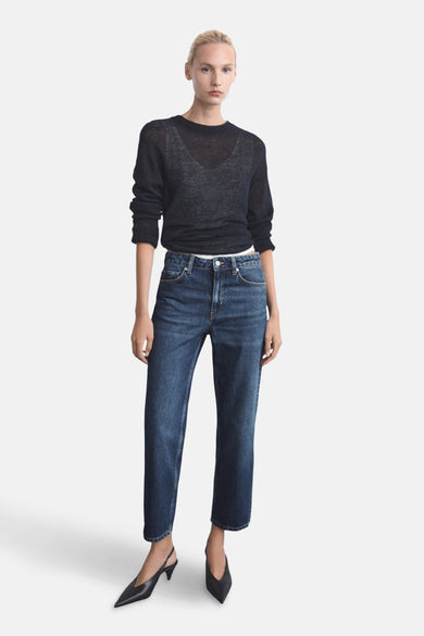 Donkerblauwe rechte jeans van MANGO, gedragen met een zwarte doorschijnende trui en zwarte pumps.