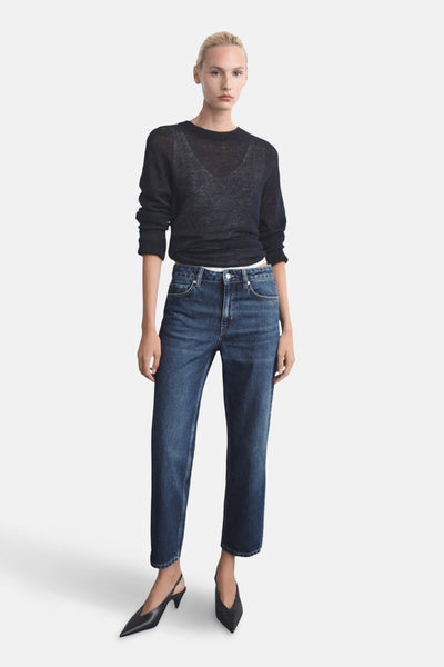 Donkerblauwe rechte jeans van MANGO, gedragen met een zwarte doorschijnende trui en zwarte pumps.