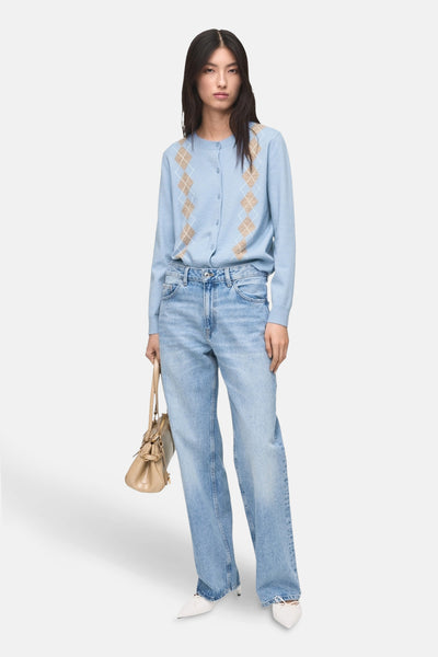 Gilet bleu à losanges par MANGO, porté avec un jean délavé, un sac beige et des escarpins blancs.