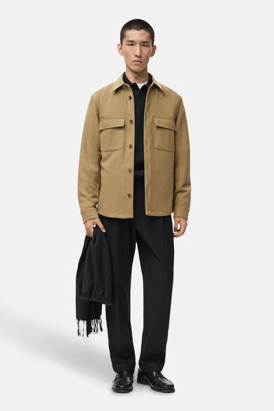 Kort bruin jasje van MANGO met klepzakken, gedragen over een zwart poloshirt, zwarte broek en leren schoenen.