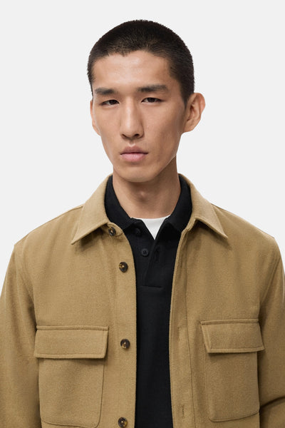 Veste courte brune de MANGO, avec poches plaquées et boutons apparents, portée sur un polo noir.