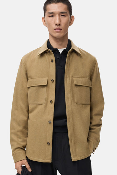 Kort bruin jasje van MANGO, met klepzakken, gedragen over een zwart poloshirt en een zwarte broek.