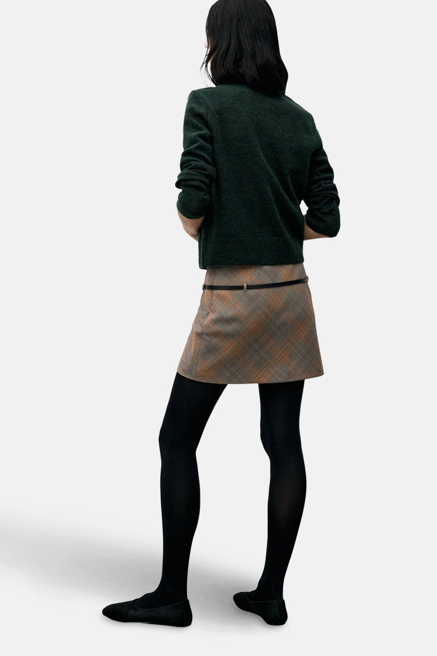 Cardigan vert par MANGO, avec une texture douce et des manches longues, porté avec une jupe à carreaux et des collants noirs.
