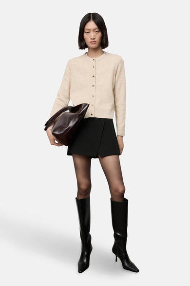 Cardigan blanc cassé by MANGO, porté avec une jupe-short noire, des collants noirs et des bottes hautes.