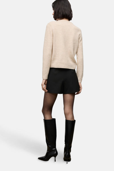Cardigan beige chiné par MANGO, porté avec un short noir, des collants noirs et des bottes en cuir noires.