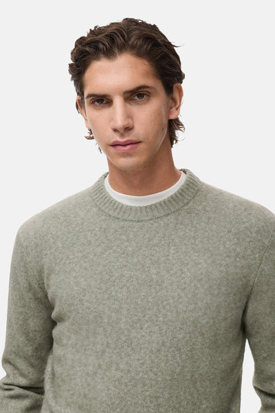 Pull col rond vert de MANGO, porté sur un t-shirt blanc, avec une texture fine et un style décontracté.
