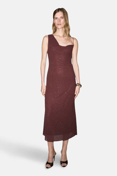 Robe bordeaux à une épaule par MANGO, ornée de motifs pointillés scintillants, portée avec des mules noires.
