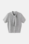 Gilet gris de MANGO, à manches courtes avec une encolure à nouer et une fermeture boutonnée.