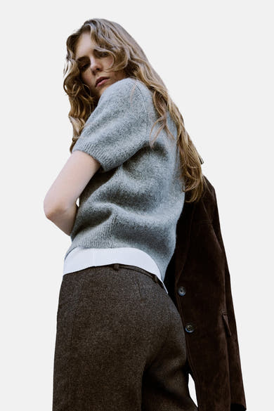 Gilet gris de MANGO, porté avec un pantalon brun texturé et une veste en daim marron.
