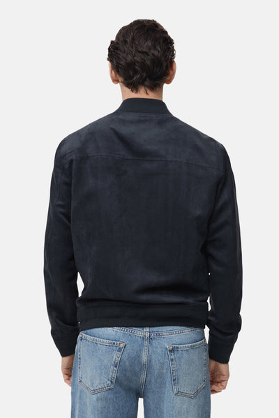 Veste courte bleu marine de MANGO, avec texture suédée, coupe bomber et poches arrière sur un jean bleu clair.