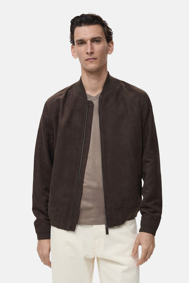 Veste courte marron de MANGO, avec une texture suédée, portée sur un t-shirt beige et un pantalon blanc cassé.