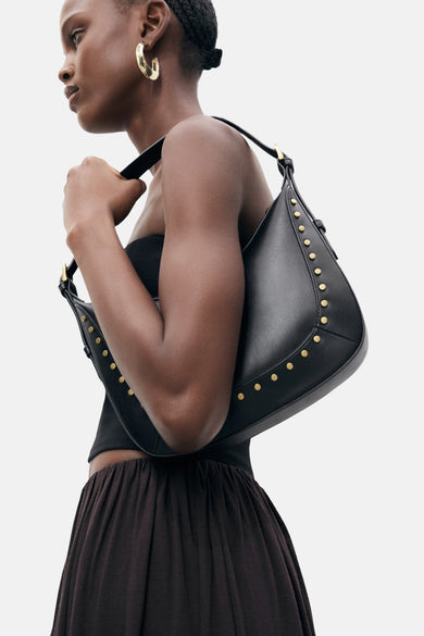 Zwarte leren schoudertas met studs van Mango, gedragen over de schouder, met een zwarte bustier en een bruine rok.