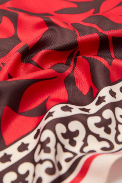 Foulard rouge en soie, de MANGO, à motifs floraux et bordure ornementale, avec un effet de tissu froissé.
