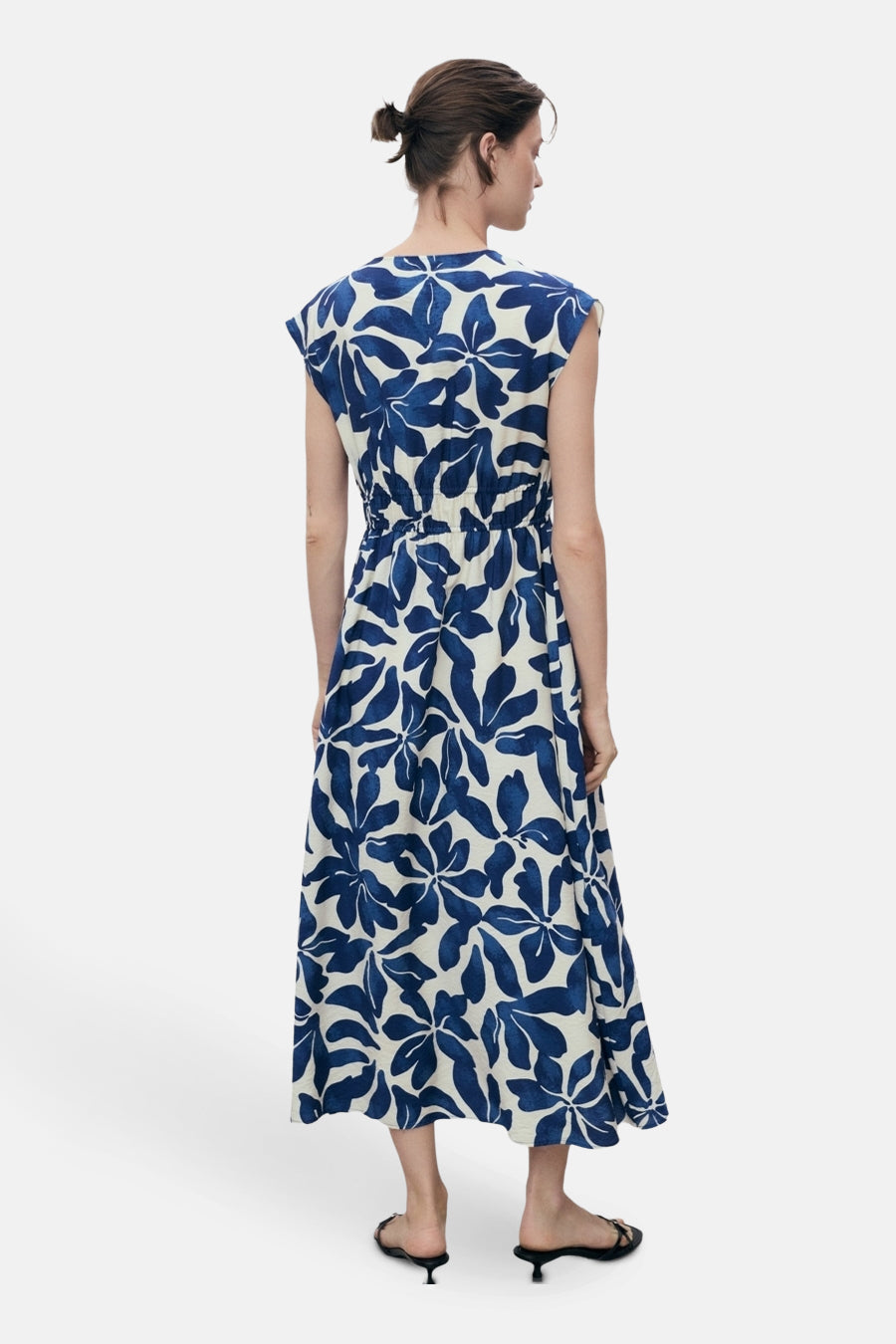 Lange blauwe jurk met bloemenprint van MANGO, met een elastische taille en zwarte sandalen met lage hak.