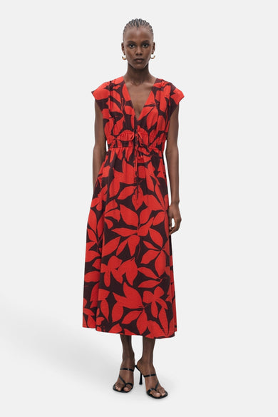 Robe rouge à motif floral par MANGO, avec une taille cintrée à cordon et des sandales à talons noirs.
