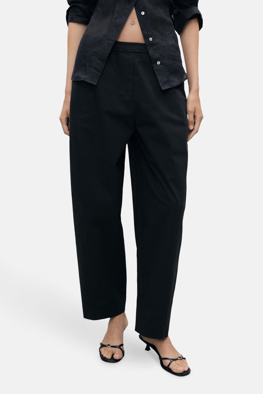 Zwarte broek van MANGO, rechte pasvorm met elastische tailleband, gedragen met een open zwart overhemd.
