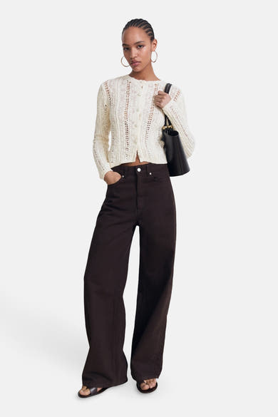 Ecru vest van MANGO met ajourpatroon, gedragen met een bruine high-waist jeans en platte sandalen.