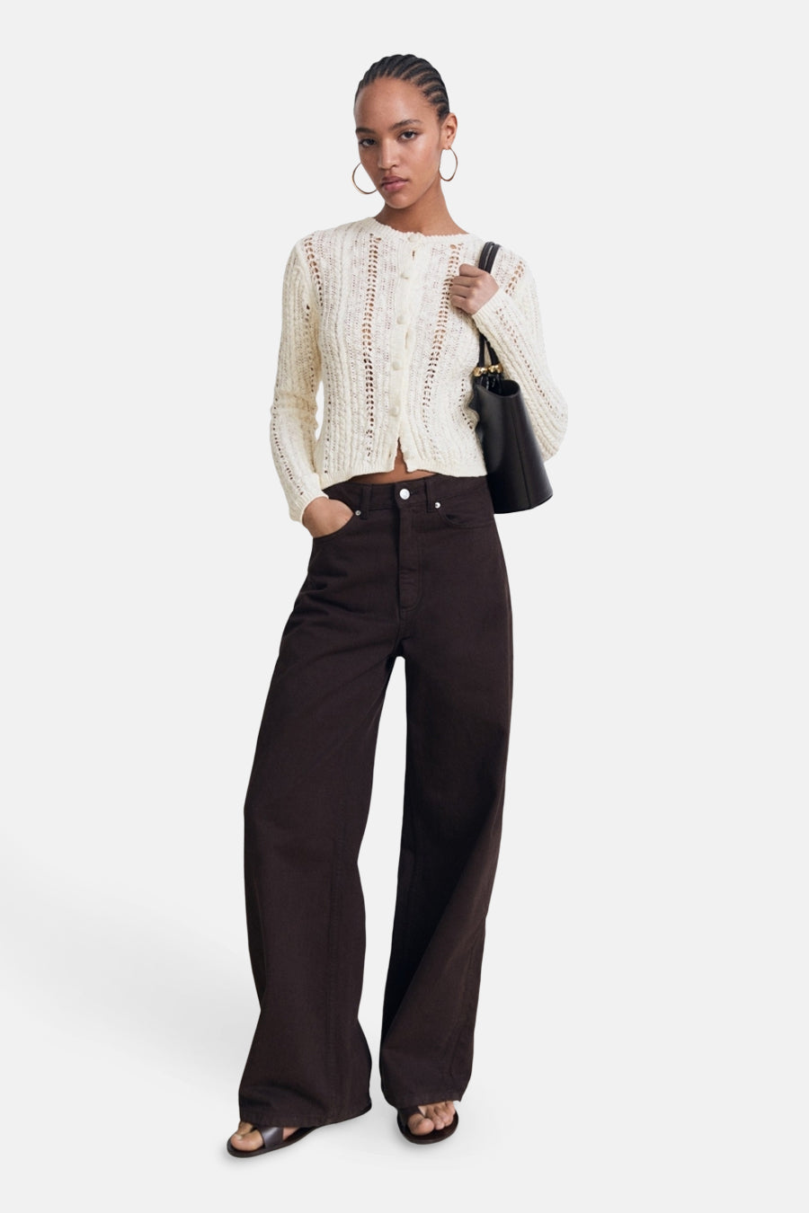 Ecru vest van MANGO met ajourpatroon, gedragen met een bruine high-waist jeans en platte sandalen.