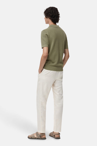 Korte mouwen poloshirt van MANGO, gedragen met een witte broek en bruine sandalen, achtergezicht.