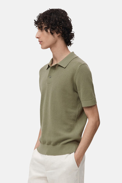 Polo kaki à manches courtes de MANGO, en maille texturée, porté avec un pantalon blanc.
