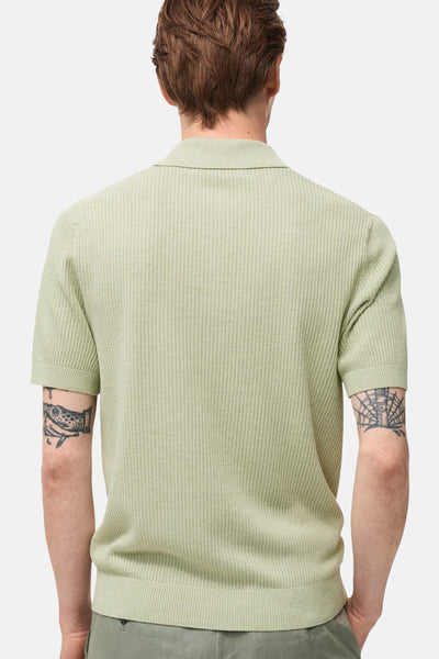 Groen poloshirt met korte mouwen van MANGO, gebreide textuur, achtergezicht, gedragen met een groene broek.