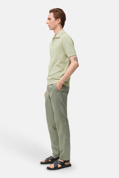 Polo à manches courtes vert de MANGO, en maille côtelée, porté avec un pantalon vert et des sandales noires.
