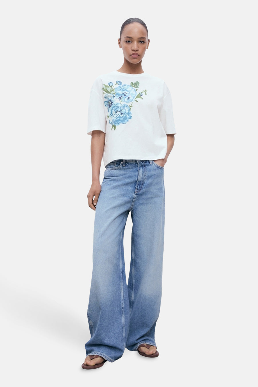 Wit meerkleurig T-shirt met korte mouwen van MANGO, met blauw bloemenpatroon op de voorkant, gedragen met een lichtblauwe wijde jeans.