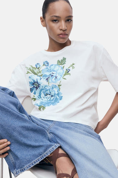 Wit T-shirt met korte mouwen van MANGO, met blauwe bloemenprint op de voorkant, gedragen met een wijde spijkerbroek.