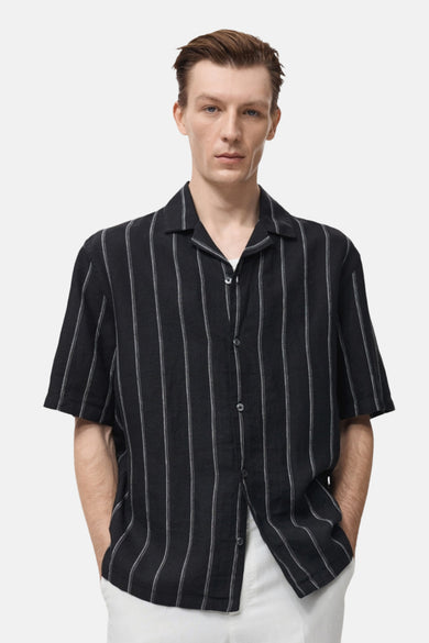 Chemise noire à rayures verticales de MANGO, portée ouverte sur un t-shirt blanc et un pantalon blanc.