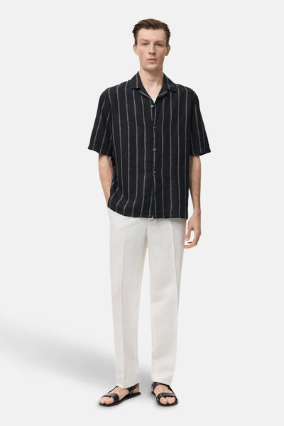 Chemise noire à rayures verticales de MANGO, portée avec un pantalon blanc et des sandales noires.