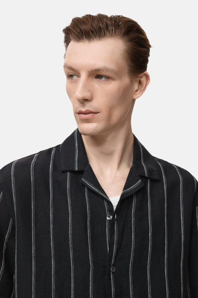 Chemise noire à rayures verticales, à manches courtes de MANGO, portée avec un t-shirt blanc.