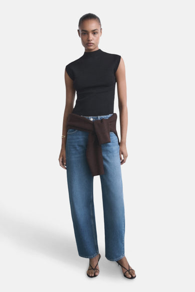 Middelblauwe jeans van MANGO, gedragen met een bruine trui die om de taille is geknoopt en sandalen met dunne bandjes.