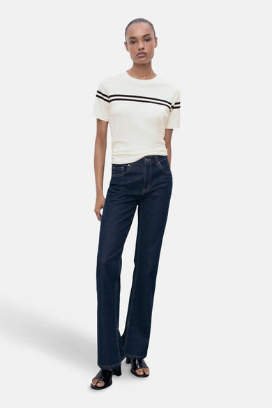 T-shirt à manches courtes blanc à rayures noires de MANGO, porté avec un jean foncé et des sandales noires.