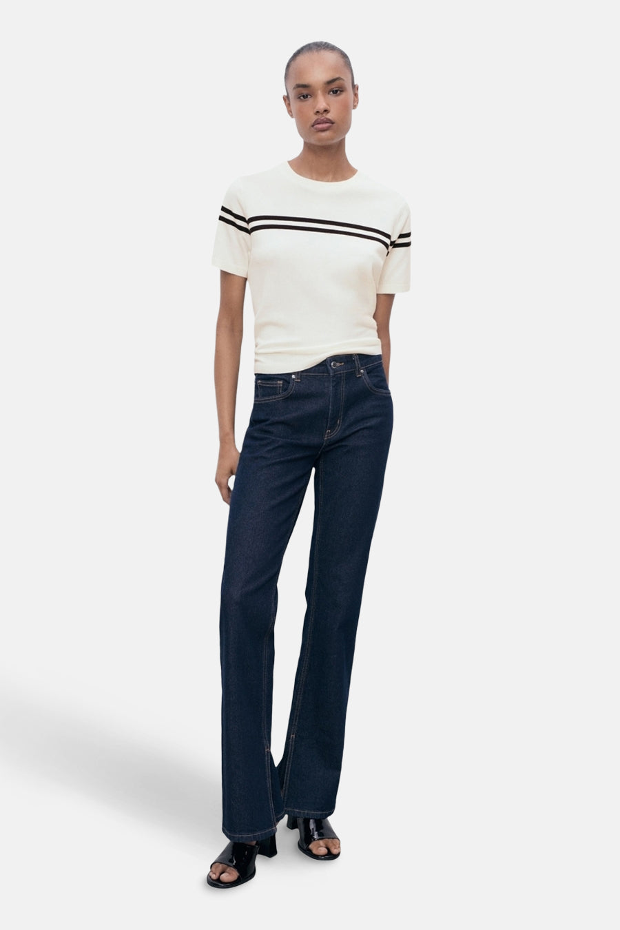 T-shirt à manches courtes blanc à rayures noires de MANGO, porté avec un jean foncé et des sandales noires.