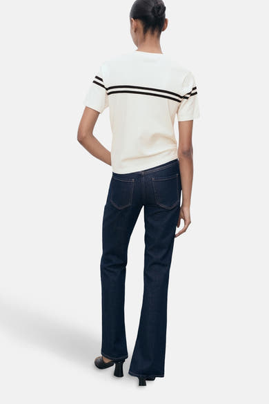T-shirt à manches courtes blanc de MANGO, rayures noires sur la poitrine, porté avec un jean bleu foncé.