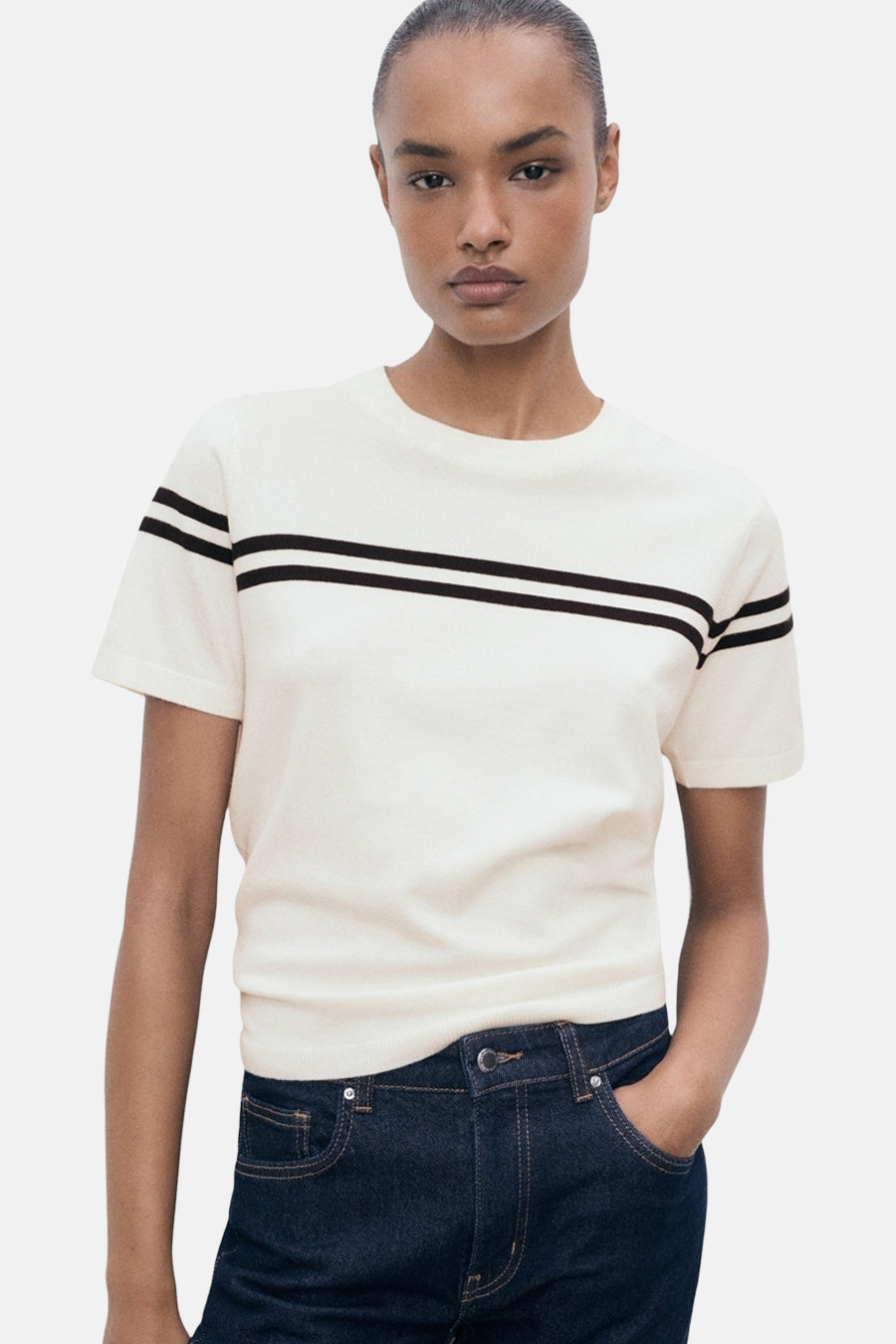 T-shirt blanc à manches courtes de MANGO, rayures horizontales noires, porté avec un jean brut.
