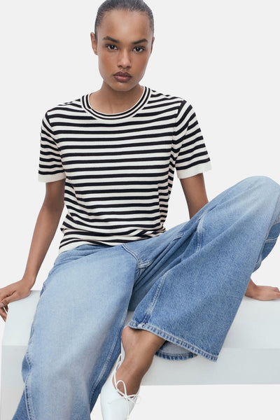 T-shirt à manches courtes rayé en maille, de MANGO, porté avec un jean large et des ballerines blanches.
