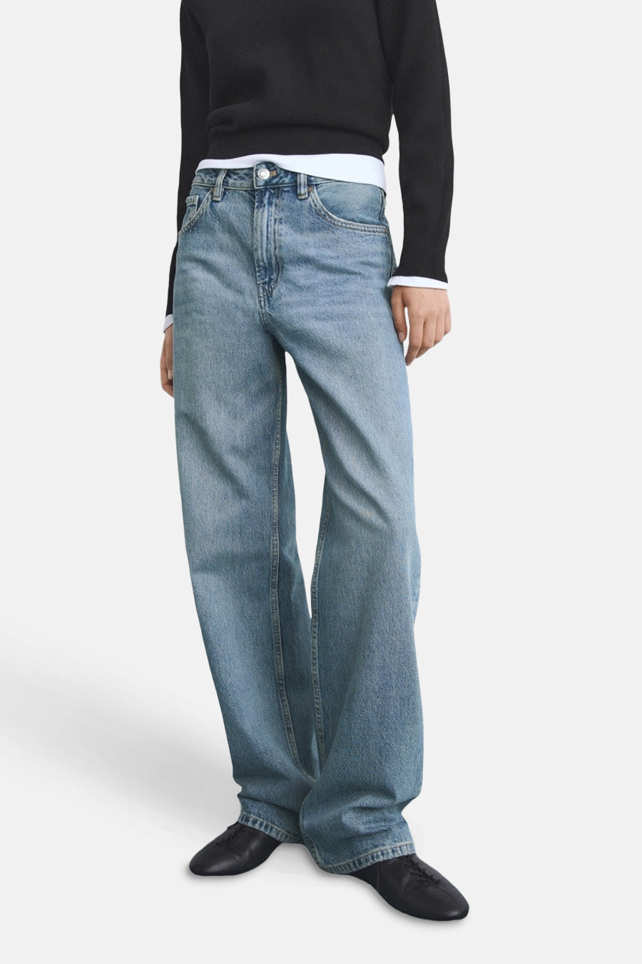 Rechte spijkerbroek in middinblauw denim van MANGO, gedragen met een zwarte trui en zwarte leren schoenen.