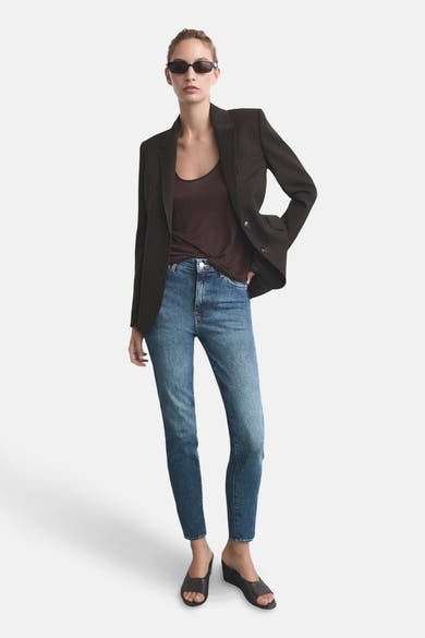 Slim jeans in medium blue denim van MANGO, gedragen met een bruin T-shirt en een donkere blazer.