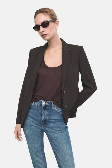 Middelblauwe spijkerbroek van MANGO, gedragen met een bruine blazer en een zwarte zonnebril.